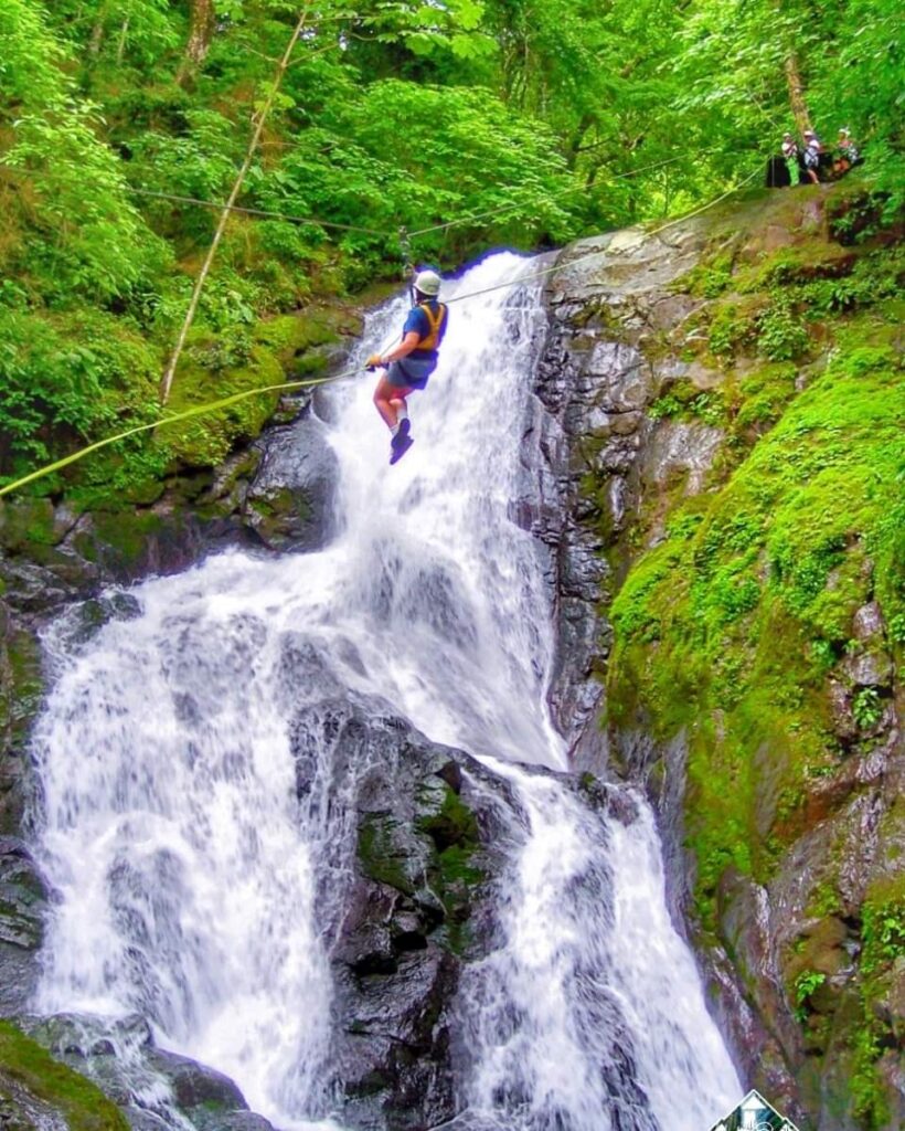 Adventurer soaring across a zipline directly above a thundering waterfall on the ultimate day trip from Jaco, Costa Rica.